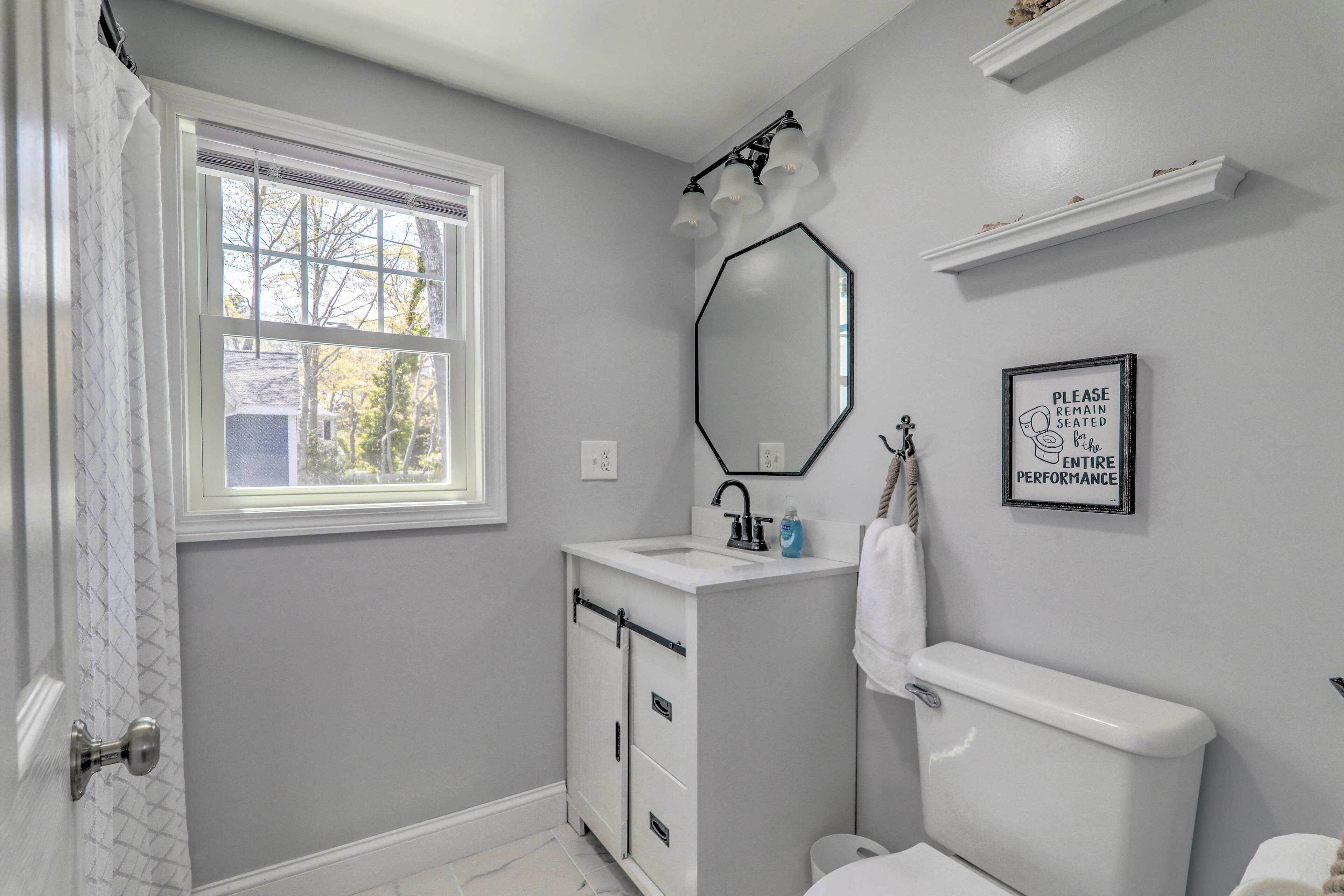 A bathroom with a window, a sink, a toilet, and a mirror.