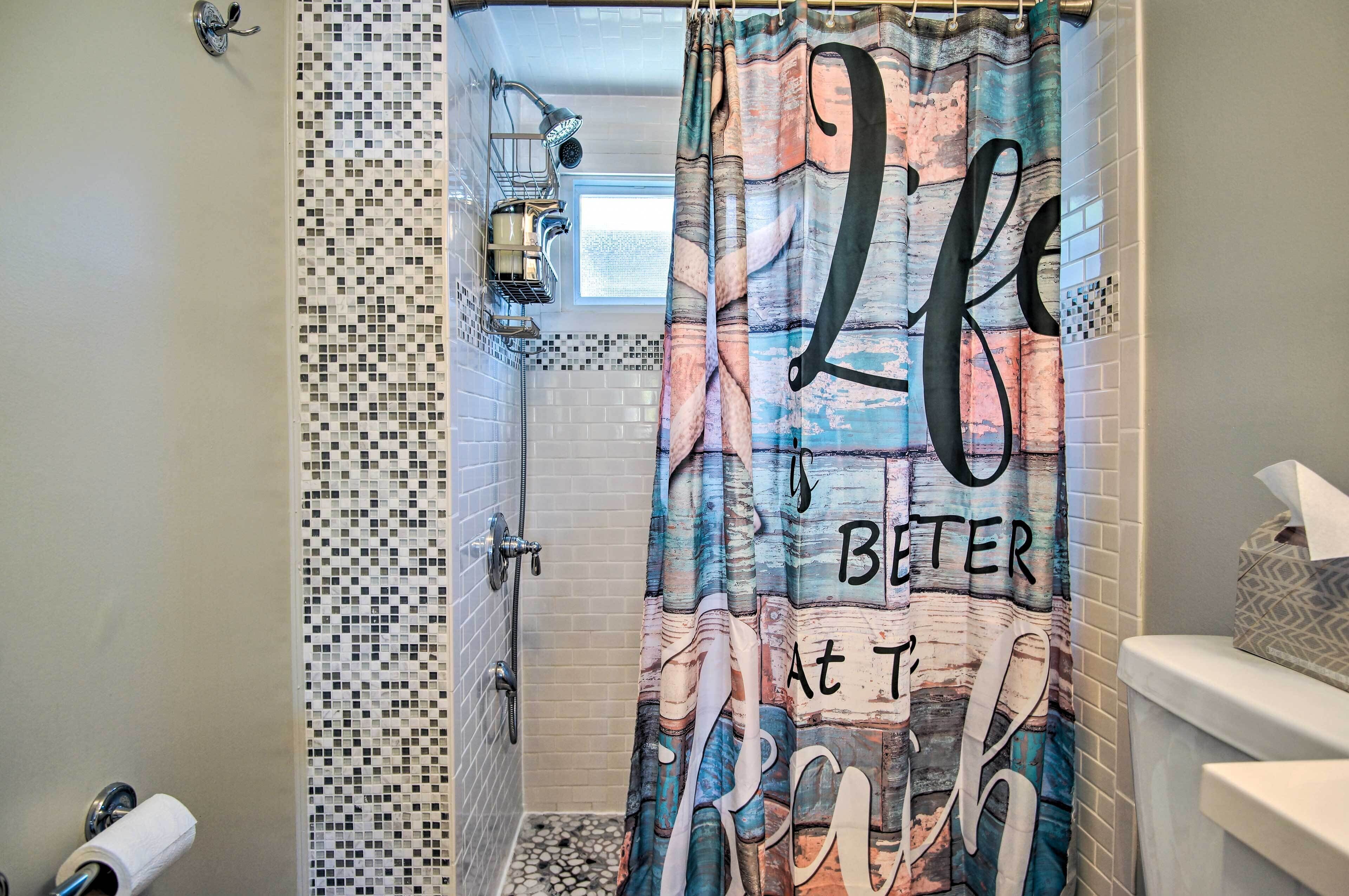 A bathroom with a shower curtain featuring a large 'LIFE' text, a showerhead, and a tiled wall.