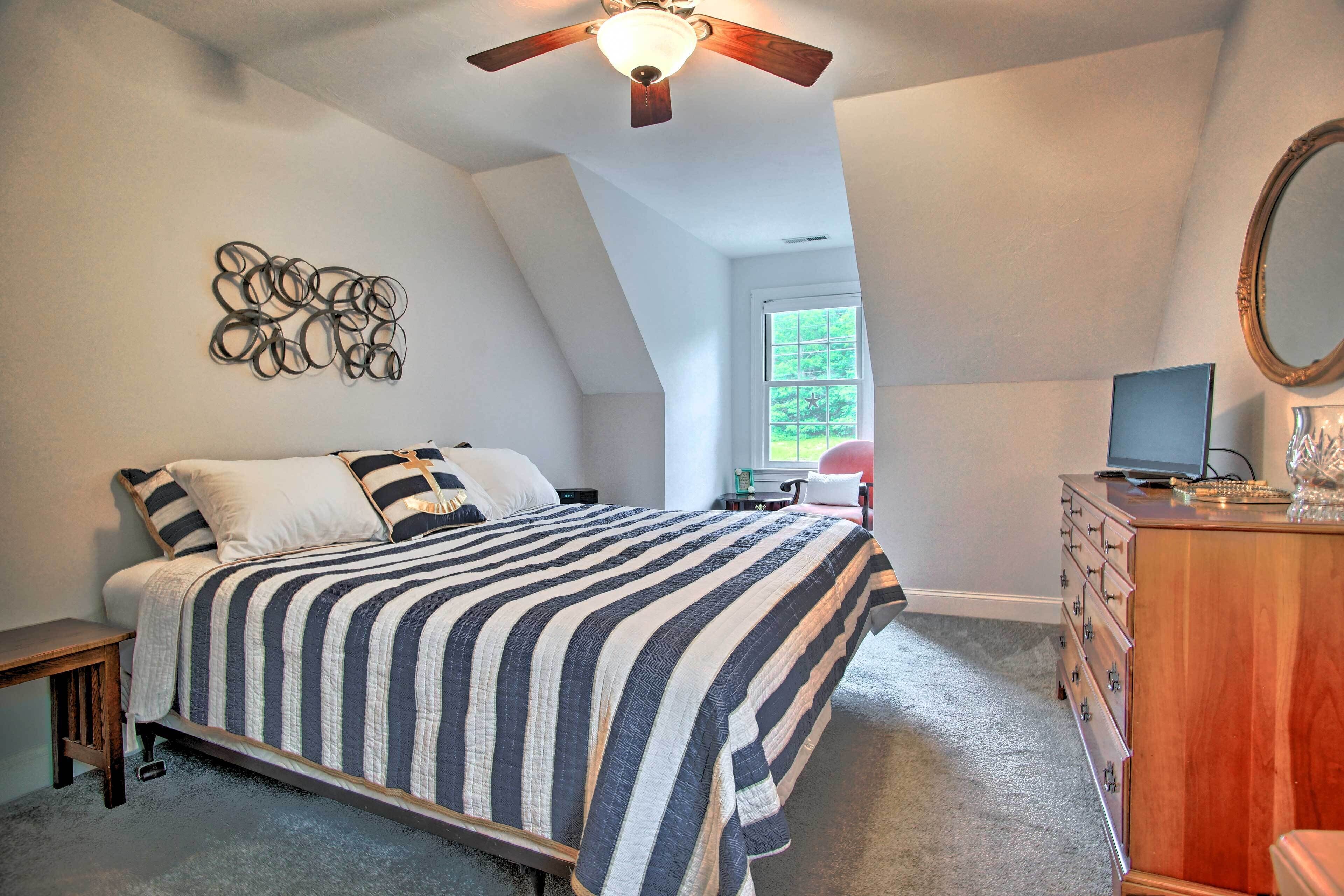 A bedroom with a bed, a wooden dresser, a ceiling fan, and a wall-mounted mirror.