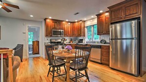 A modern kitchen with wooden cabinets, stainless steel appliances, and a dining area with a wooden table and chairs. - Cape Cod Home w/ Deck ~ 3 Mi to Beaches (Buzzards Bay)