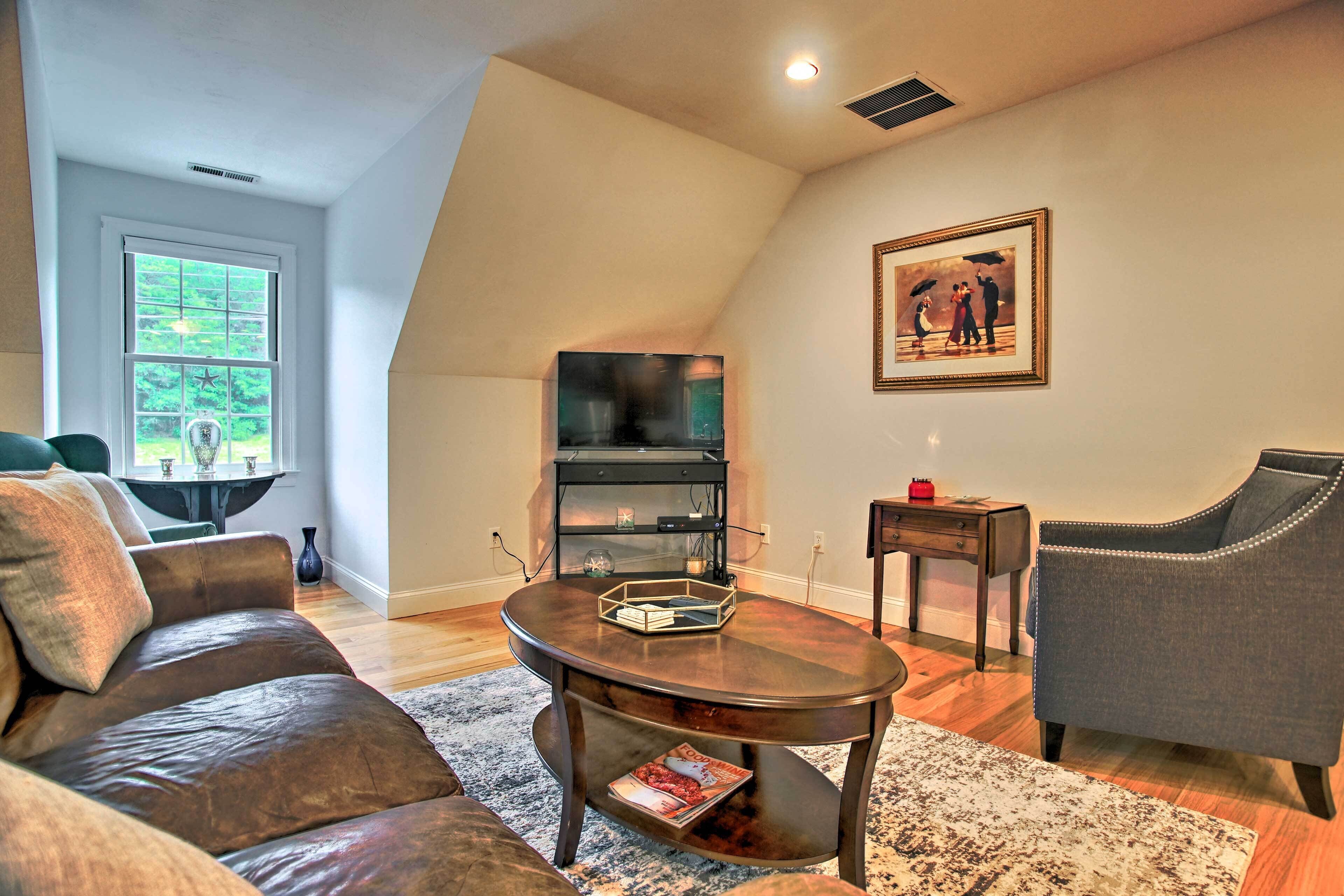 A living room with a dark brown leather sofa, a wooden coffee table, a grey armchair, a black TV stand, and a framed picture on the wall.