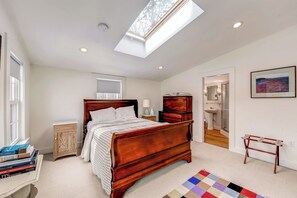 A bedroom with a wooden bed, a skylight, a bedside table, a nightstand, and a colorful rug. - Ipswich Cottage: Beautiful Views, 5 Mins to Beach (Ipswich)
