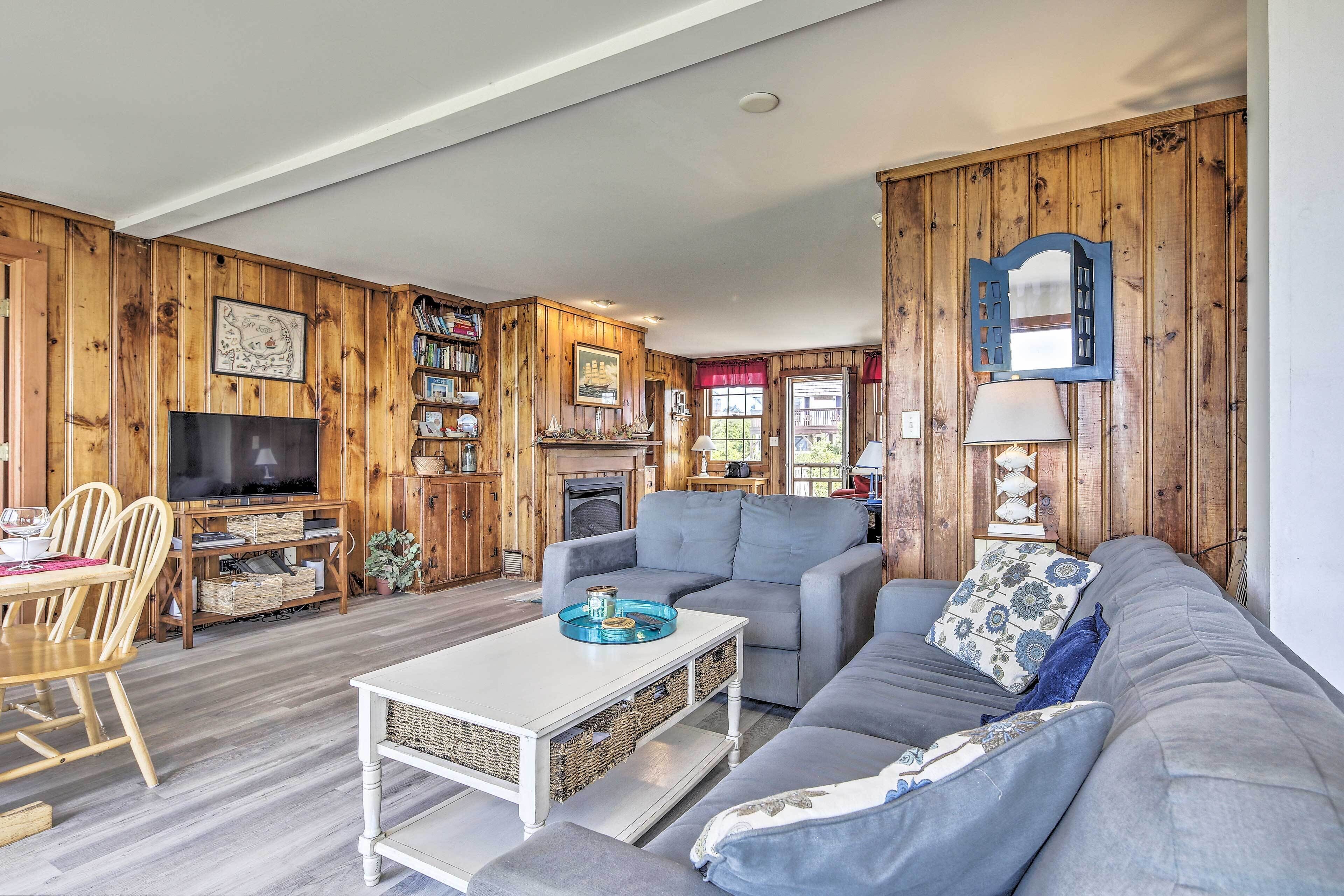 Ein gemütliches Wohnzimmer mit grauem Sofa, einem weißen Couchtisch, Holzvertäfelung, einem Kamin und einem Fernseher.