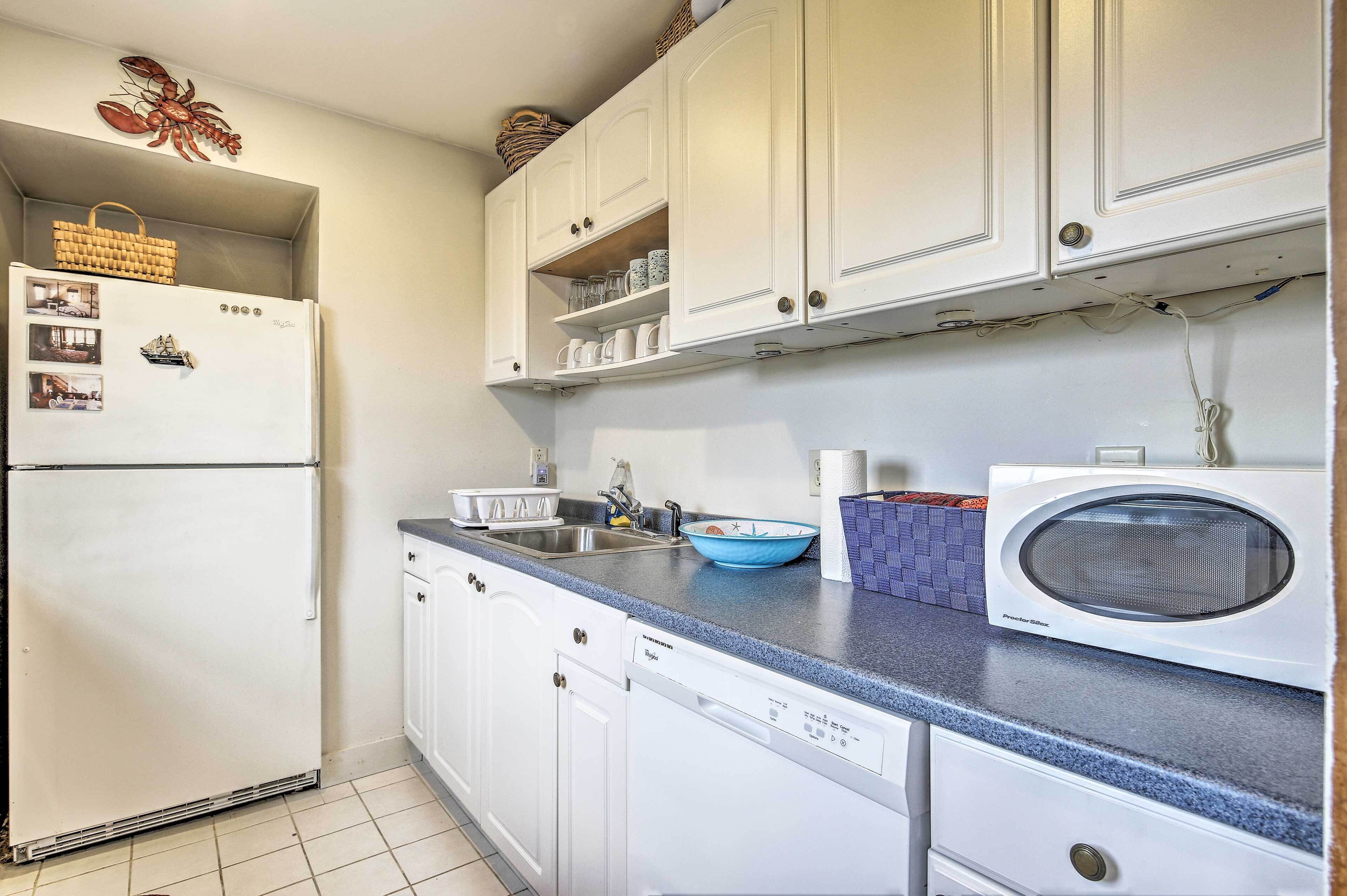 Una cocina con armarios blancos, un refrigerador, un lavavajillas, un fregadero y un microondas.