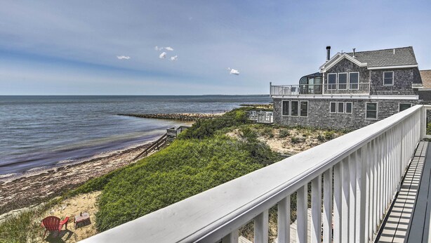 A coastal house with a deck overlooking the beach and ocean. - Fireplace + Sunroom! Oceanfront Cape Cod Cottage (Dennis Port)