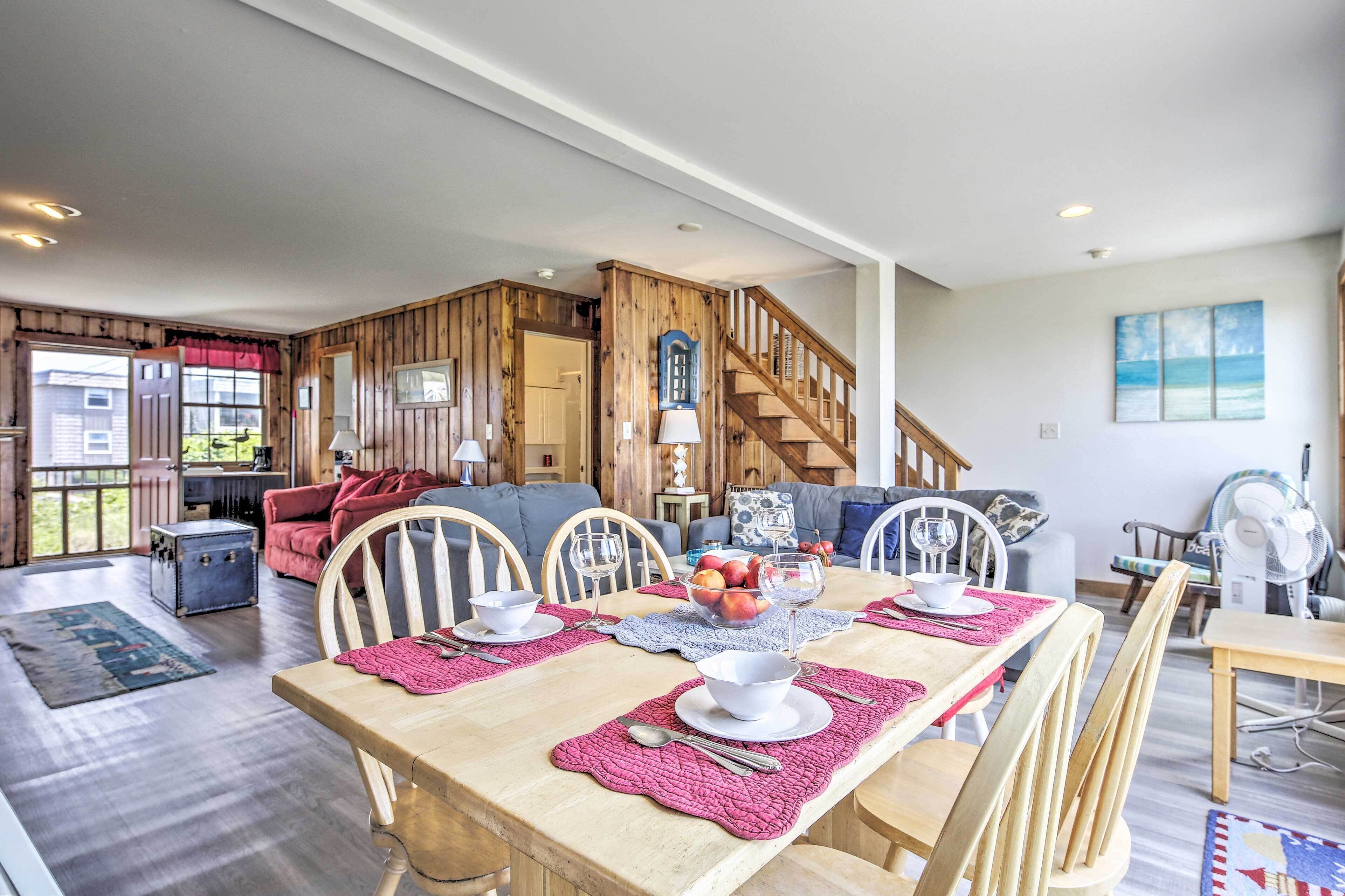 A spacious living area with a wooden dining table set for four, a staircase, and a view of the outdoors.