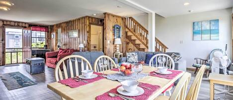 A spacious living area with a wooden dining table set for four, a staircase, and a view of the outdoors.