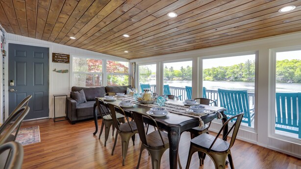 Comedor con techo de madera, grandes ventanales con vista al agua, árboles y un muelle.