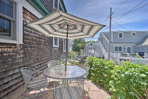 Une terrasse avec une table ronde et des chaises, un parasol et une clôture blanche en bois.