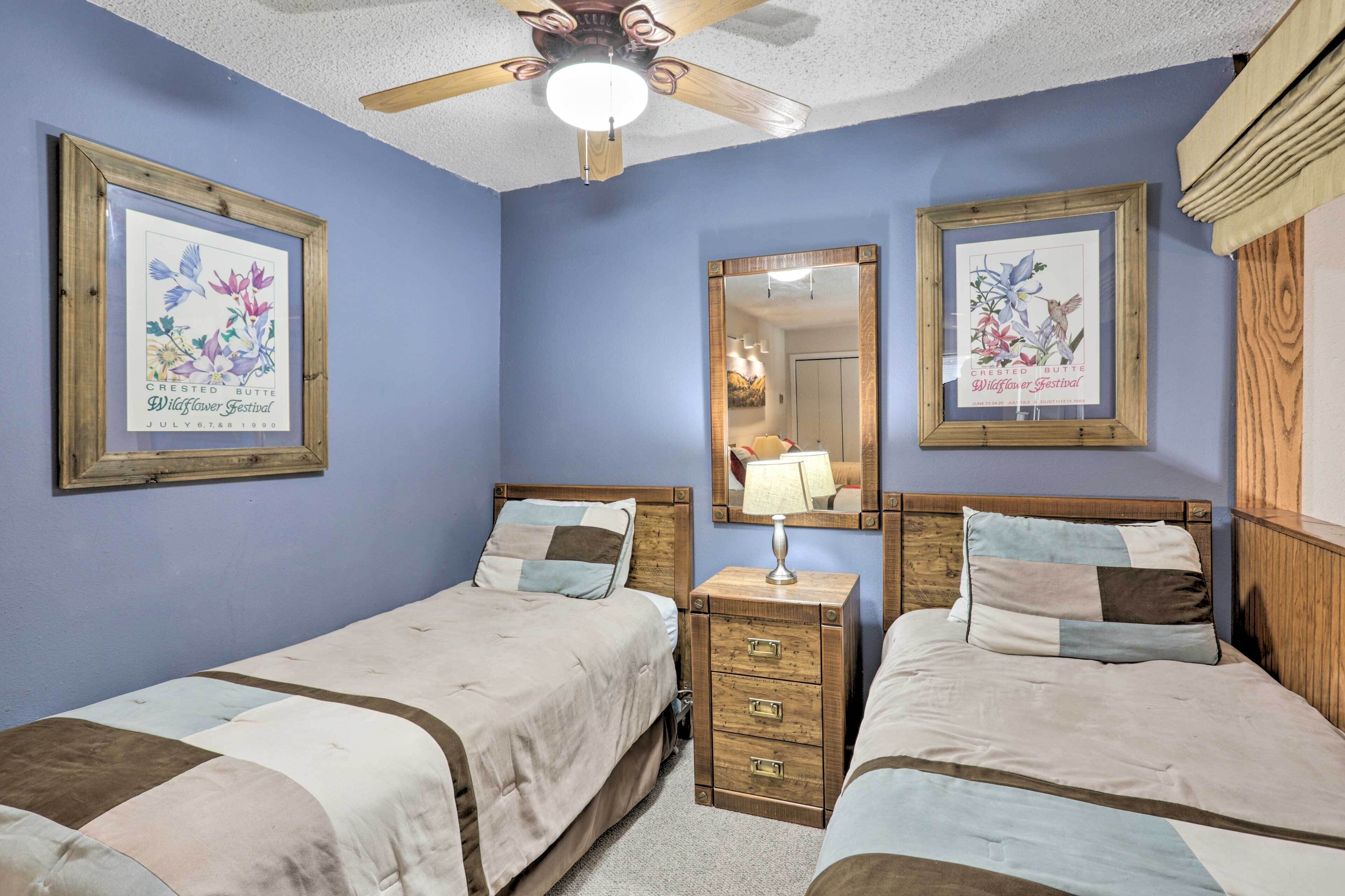 A bedroom with two beds, a nightstand, a mirror, and a ceiling fan.