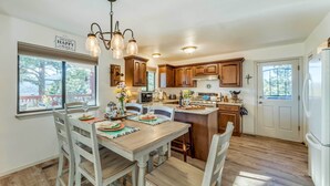 A kitchen with wooden cabinets, a dining table with chairs, a chandelier, and a refrigerator. - Wildlife Watching & Mtn Views: Luxe Ruidoso Escape (Ruidoso)