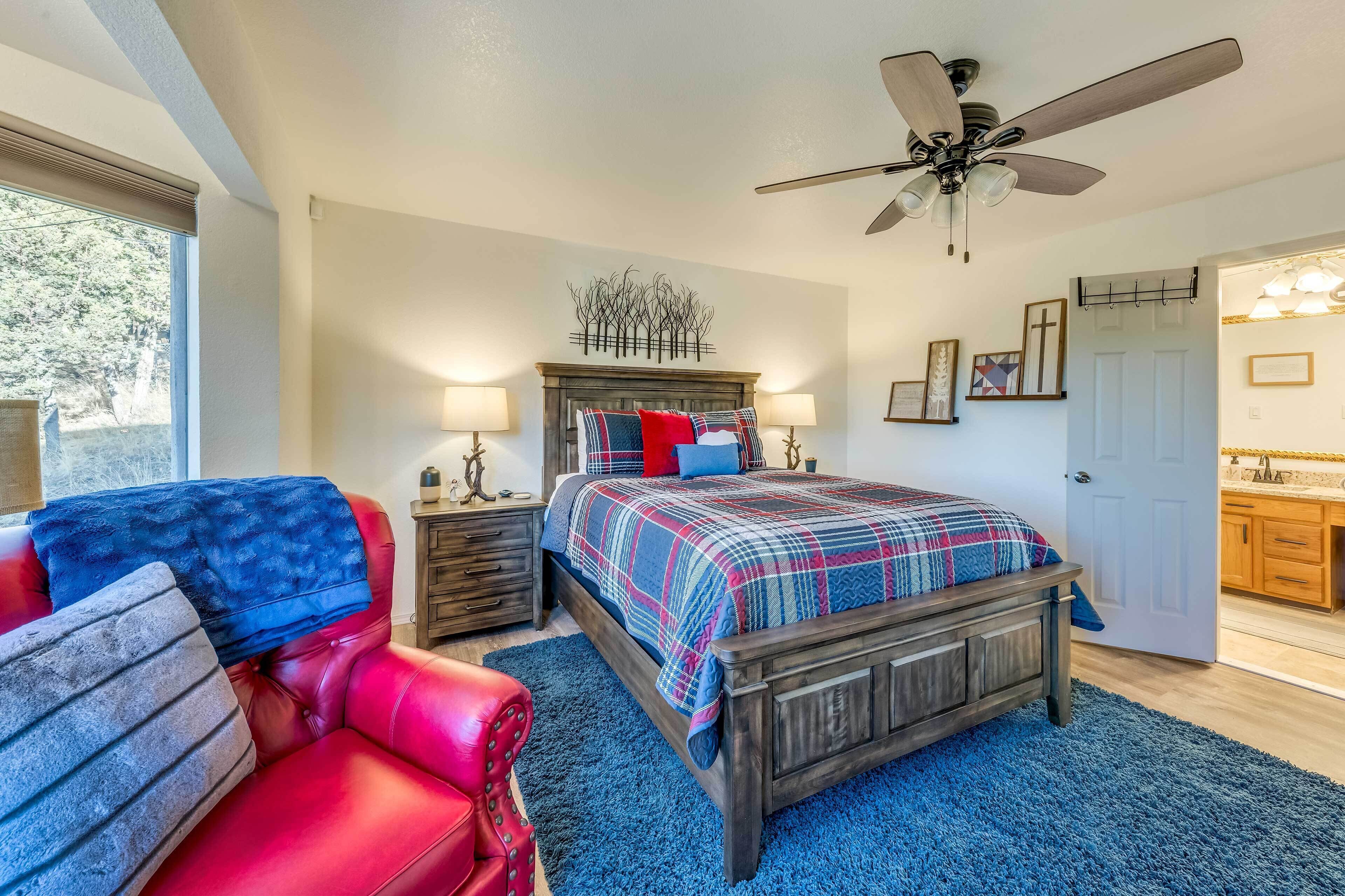 A bedroom with a bed, a red chair, a ceiling fan, and a door leading to a bathroom.