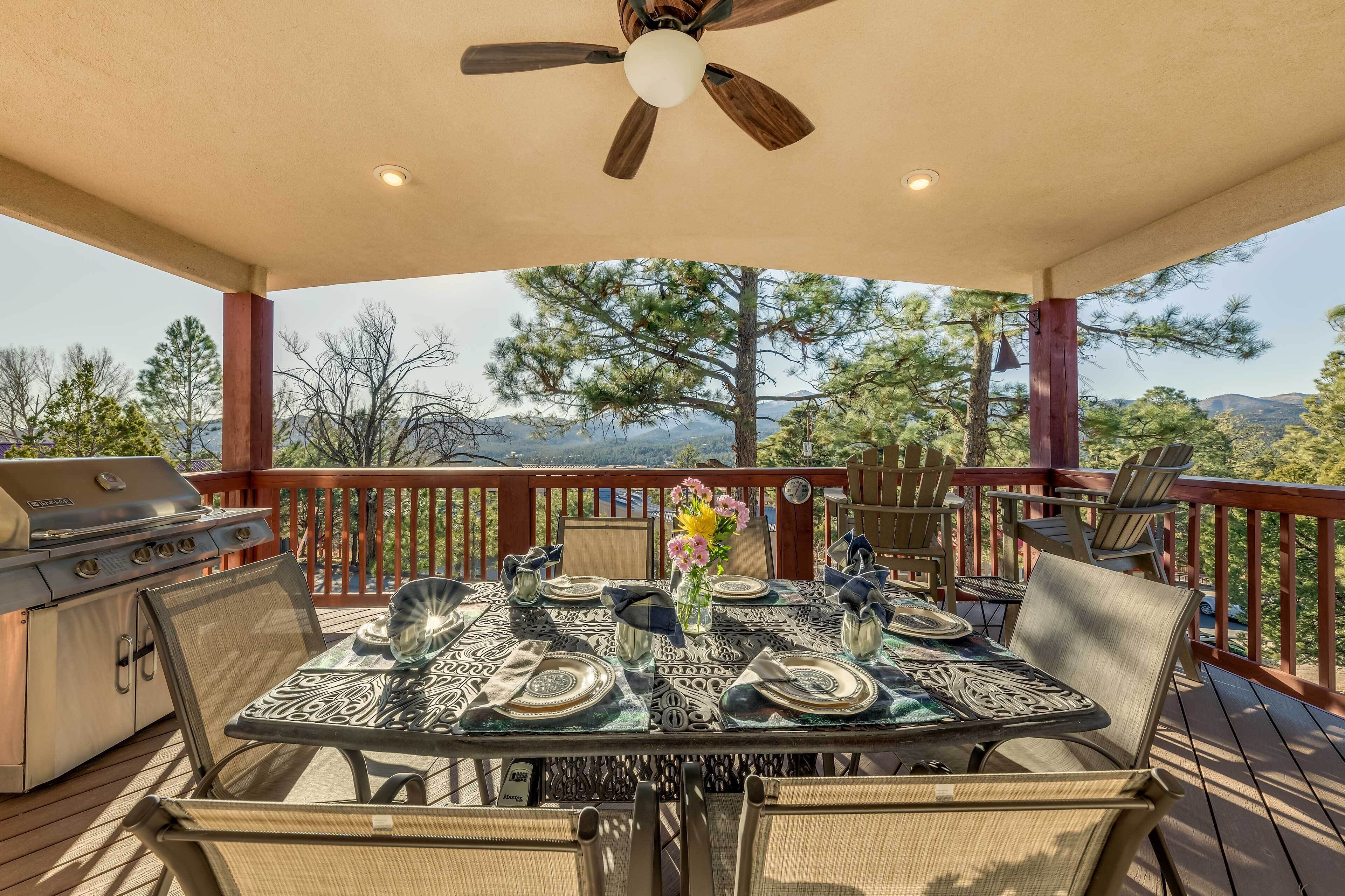 A covered outdoor deck with a table set for dining, a grill, and a ceiling fan.