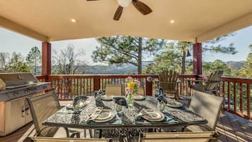 A covered outdoor deck with a table set for dining, a grill, and a ceiling fan.