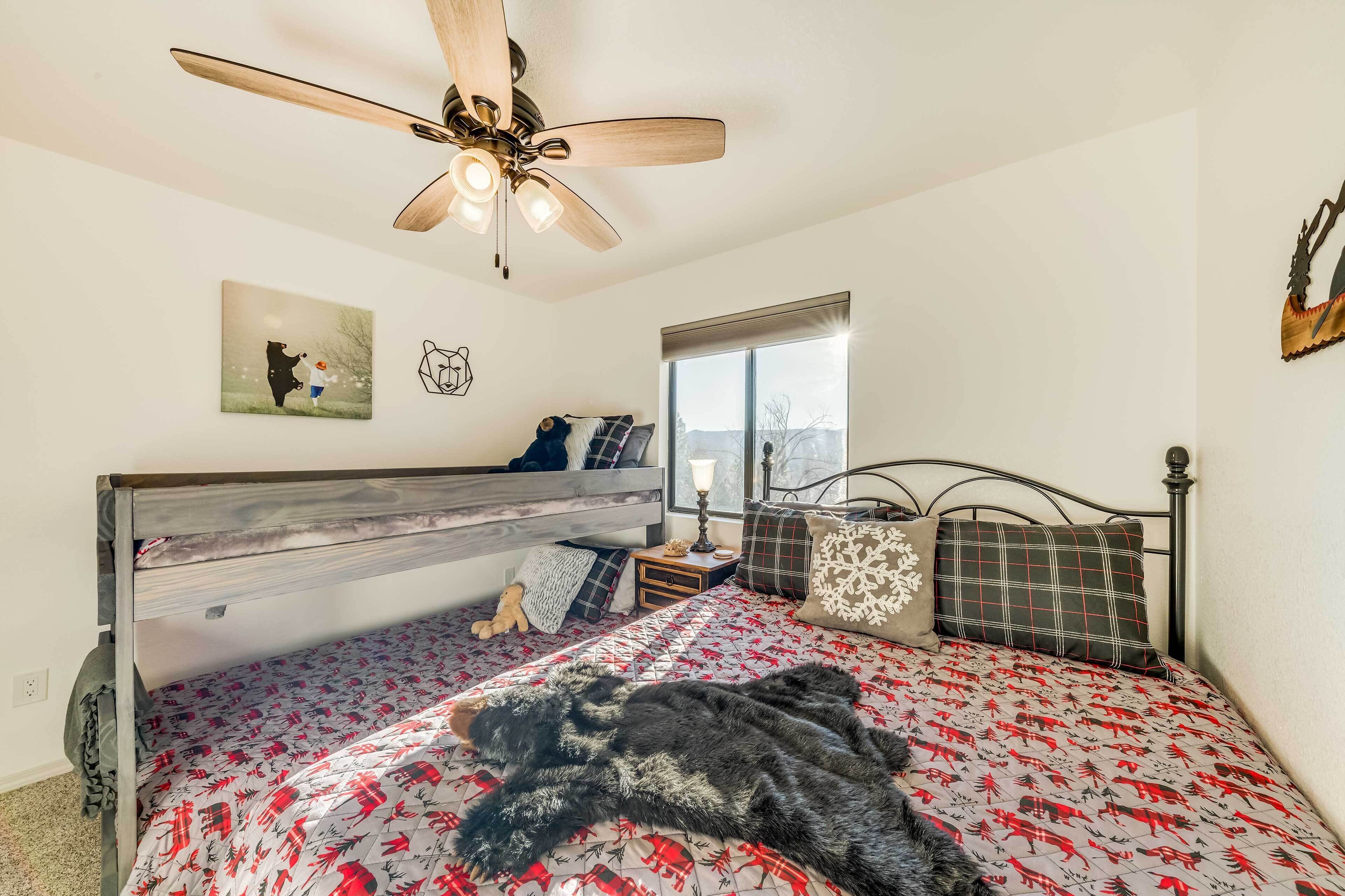 A bedroom with a wooden bunk bed, a ceiling fan, a window with a view, and a bear-themed bedspread.