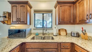 A kitchen with wooden cabinets, a stainless steel sink, a microwave, and a window with a view of trees. - Wildlife Watching & Mtn Views: Luxe Ruidoso Escape (Ruidoso)