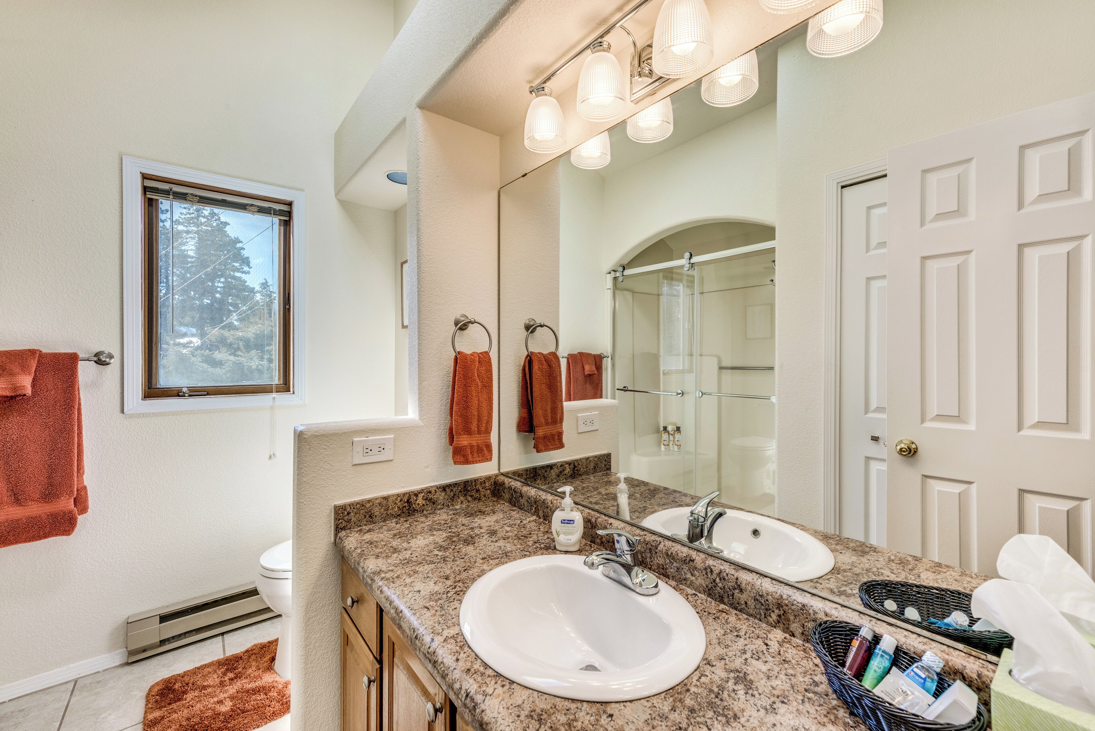 A bathroom with a white sink, a large mirror, and a window with a view of trees.