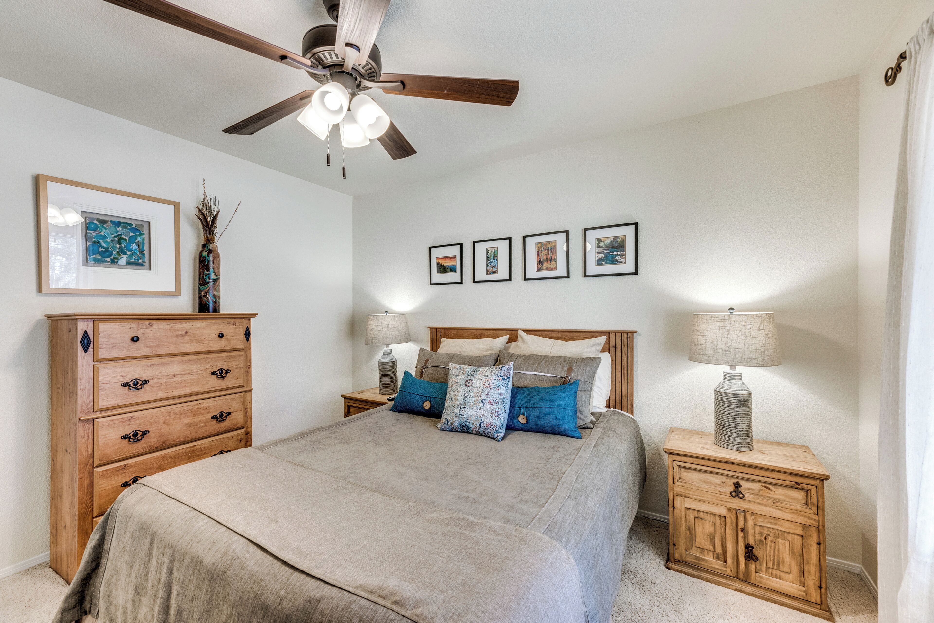 A bedroom with a bed, wooden nightstands, a dresser, a ceiling fan, and framed pictures on the wall.