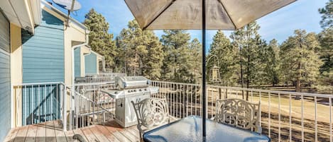 A deck with a grill, outdoor table, and umbrella.