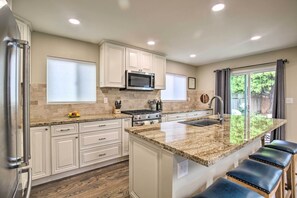 A kitchen with white cabinets, a granite countertop, a built-in microwave, a stove, and a large island with bar stools. - Coastal Carlsbad Home: 1 Mi to Beach & Downtown (Carlsbad)