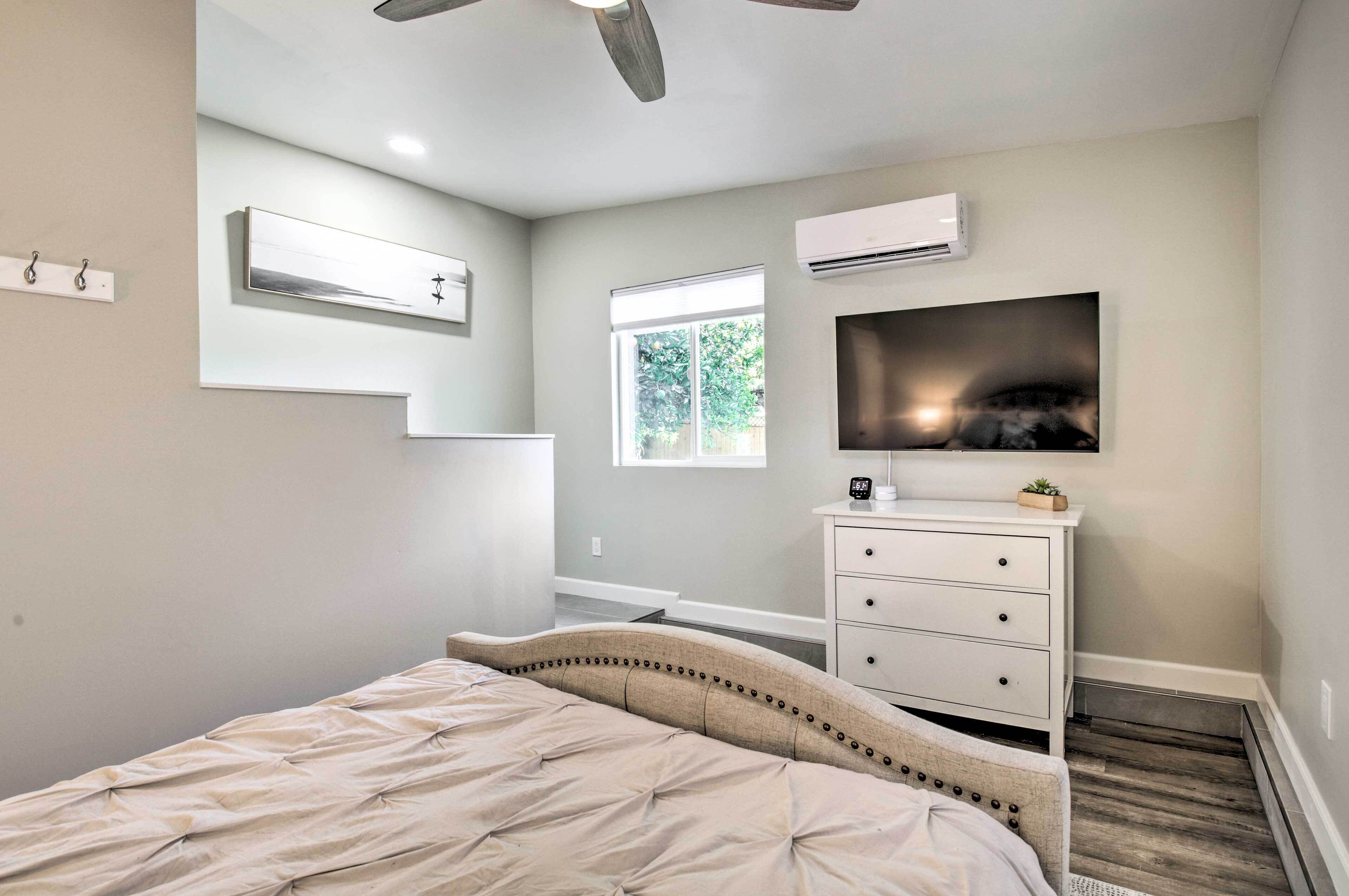 A bedroom with a bed, a dresser, an air conditioning unit, a window, and a ceiling fan.
