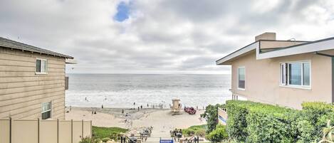 A beach view from a building with a concrete pathway leading to the shore, a lifeguard tower, and a sign with beach rules.