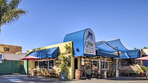 A restaurant with outdoor seating, a blue awning, and a sign advertising seafood, pizza, and pasta. - Coastal Carlsbad Home: 1 Mi to Beach & Downtown (Carlsbad)