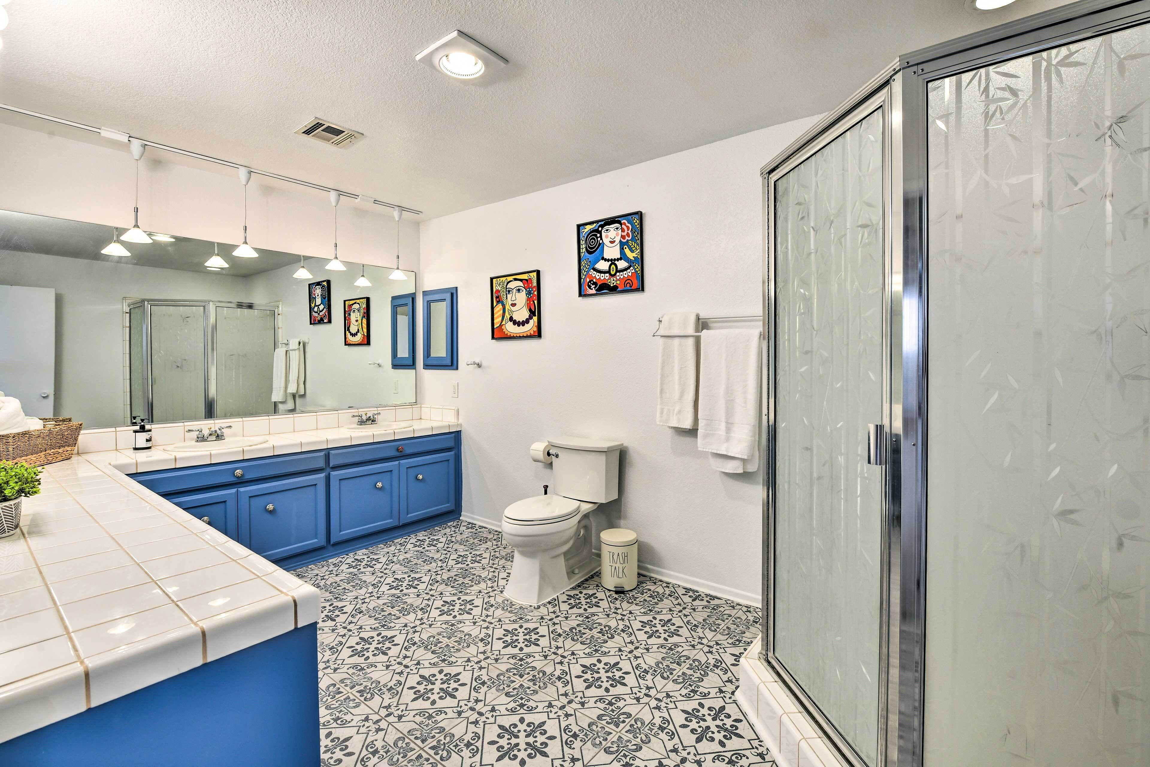 Ein Badezimmer mit einer weißen Toilette, blauen Schränken, einem großen Spiegel und Fliesen mit Muster.