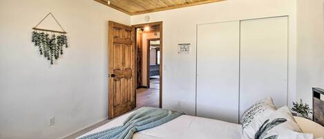 A bedroom with a bed, a ceiling fan, a wooden door, and a white wardrobe.