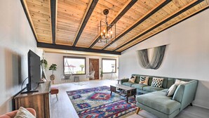 A spacious living room with a wooden ceiling, a green sofa, a patterned rug, and a television on a wooden stand. - Chic Joshua Tree Pad w/ Mountain Views & Hot Tub (Twentynine Palms)