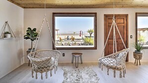 A room with two macrame chairs, a small rug, and a large window offering a view of a desert landscape. - Chic Joshua Tree Pad w/ Mountain Views & Hot Tub (Twentynine Palms)