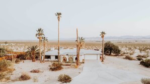 A desert landscape with a single-story building featuring arched doorways and a small attached garage. - Chic Joshua Tree Pad w/ Mountain Views & Hot Tub (Twentynine Palms)