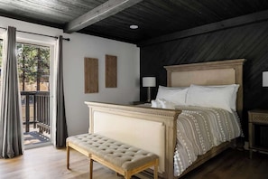 Une chambre avec un grand lit, un banc, deux lampes fixées au mur et une vue sur l’extérieur.