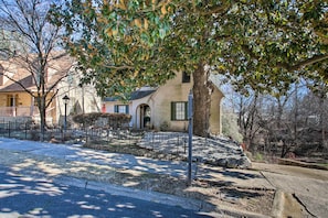 A residential property with a large tree, a paved driveway, and a stone wall.