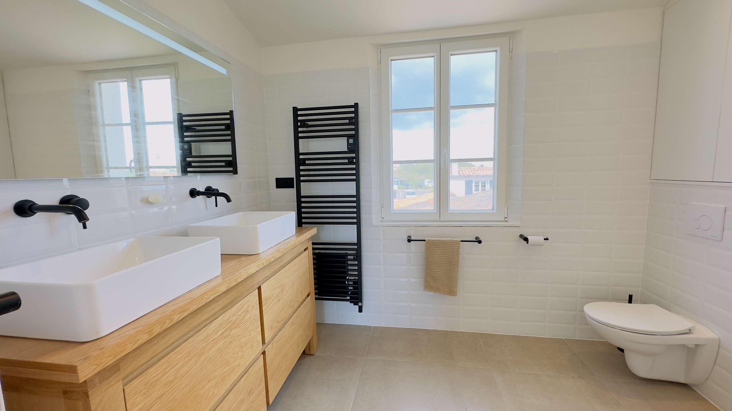 Een moderne badkamer met twee wasbakken, een spiegel, een handdoekrek en een toilet.