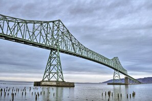 A large steel bridge spanning a body of water with a cloudy sky in the background.
