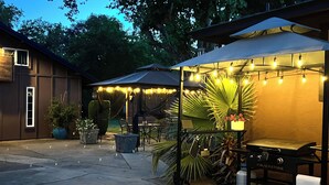 An outdoor patio area with a grill, umbrellas, string lights, and potted plants. - Private Getaway With All the Amenities (Anderson)