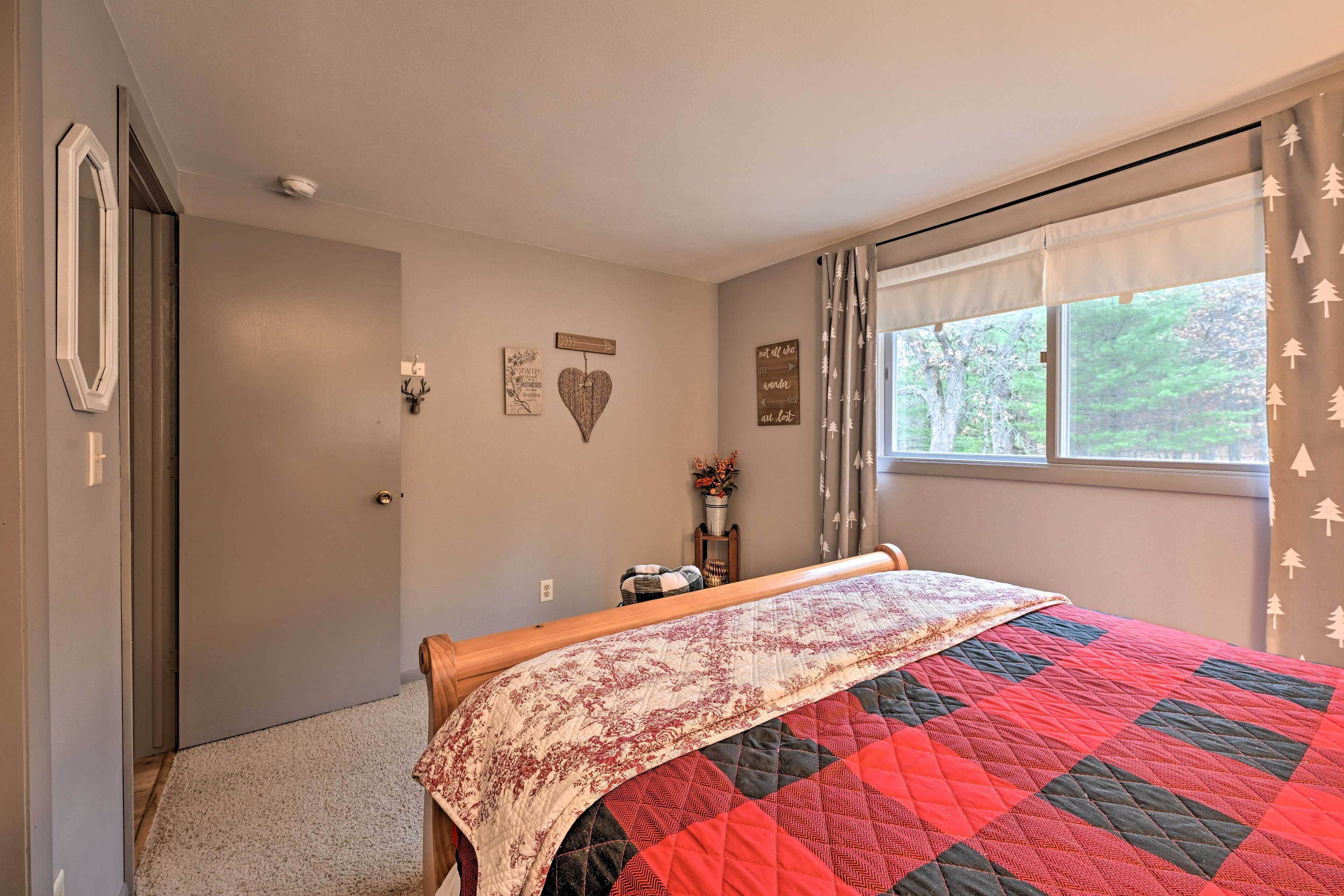 Un dormitorio con una cama cubierta por un colcha rojo y negro, una ventana con cortinas, y una pared decorada con objetos.