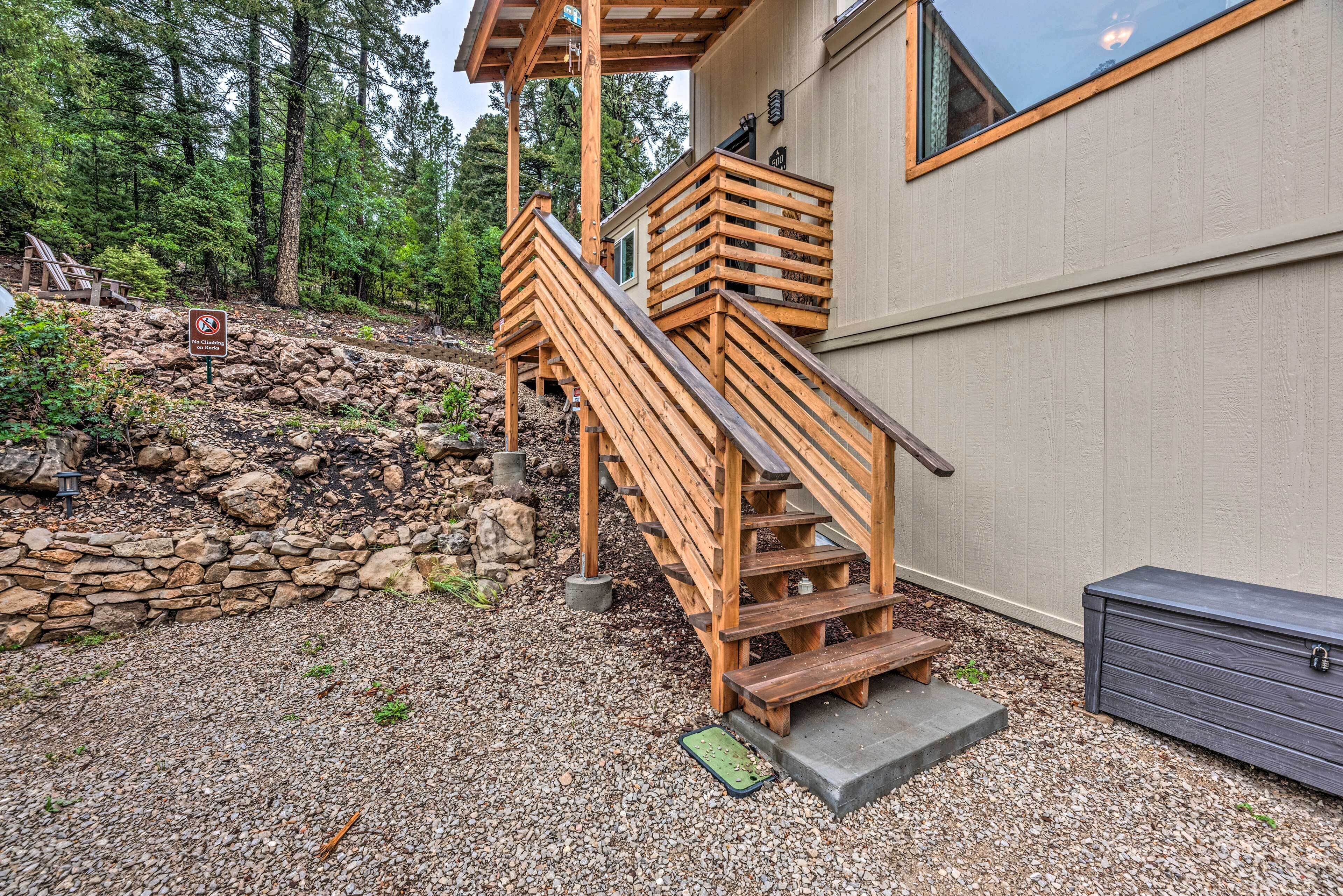 A wooden staircase leading to a house with a stone retaining wall and a view of a forested area.