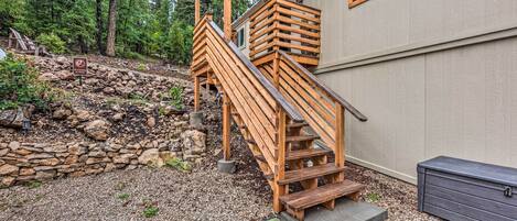 A wooden staircase leading to a house with a stone retaining wall and a view of a forested area.