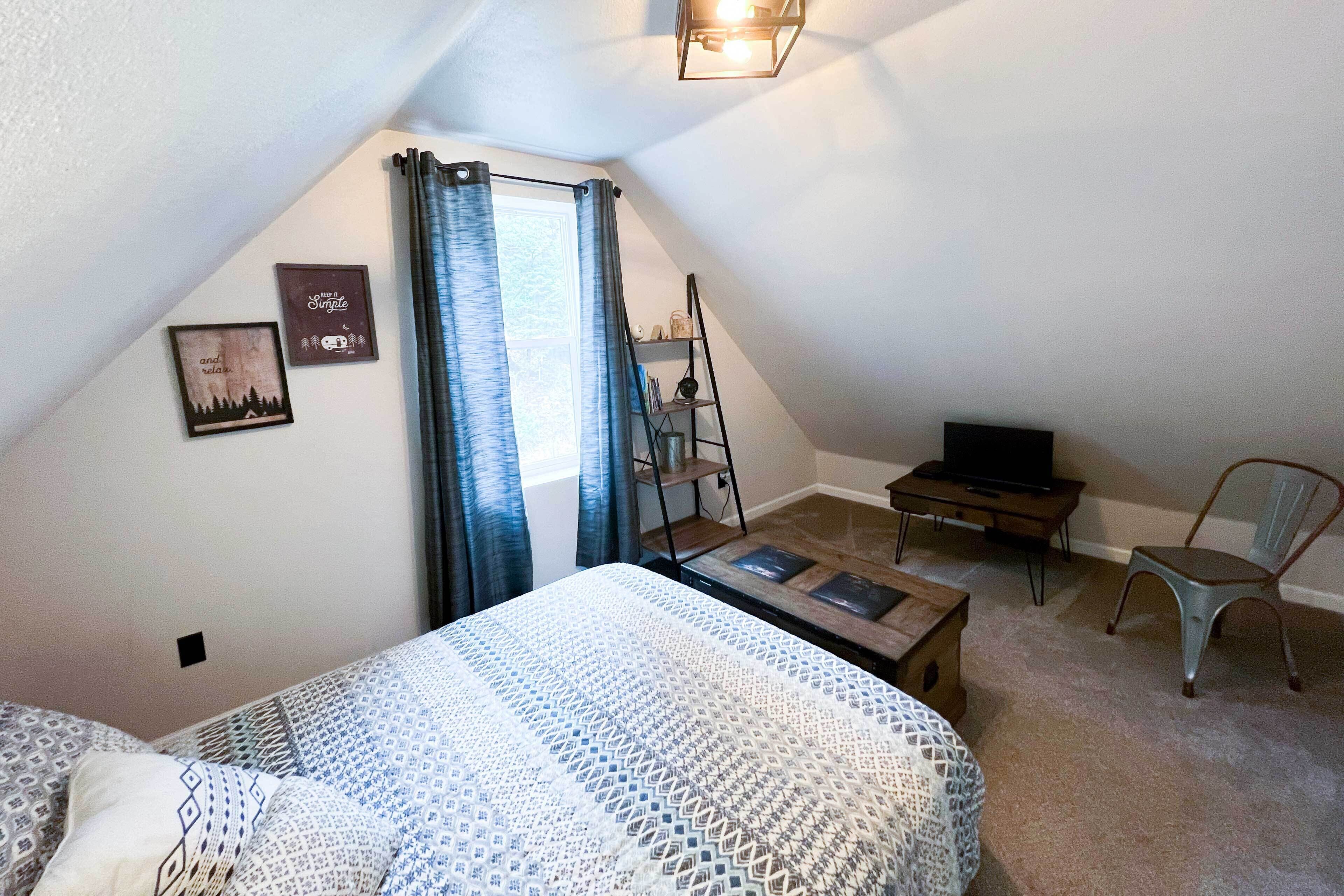Quarto de sótão aconchegante com cama, escrivaninha, cadeira e televisão.
