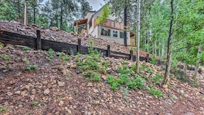 Ein modernes Haus mit einer Holzterrasse und einer Steinschmalseite, umgeben von einem Waldgebiet.