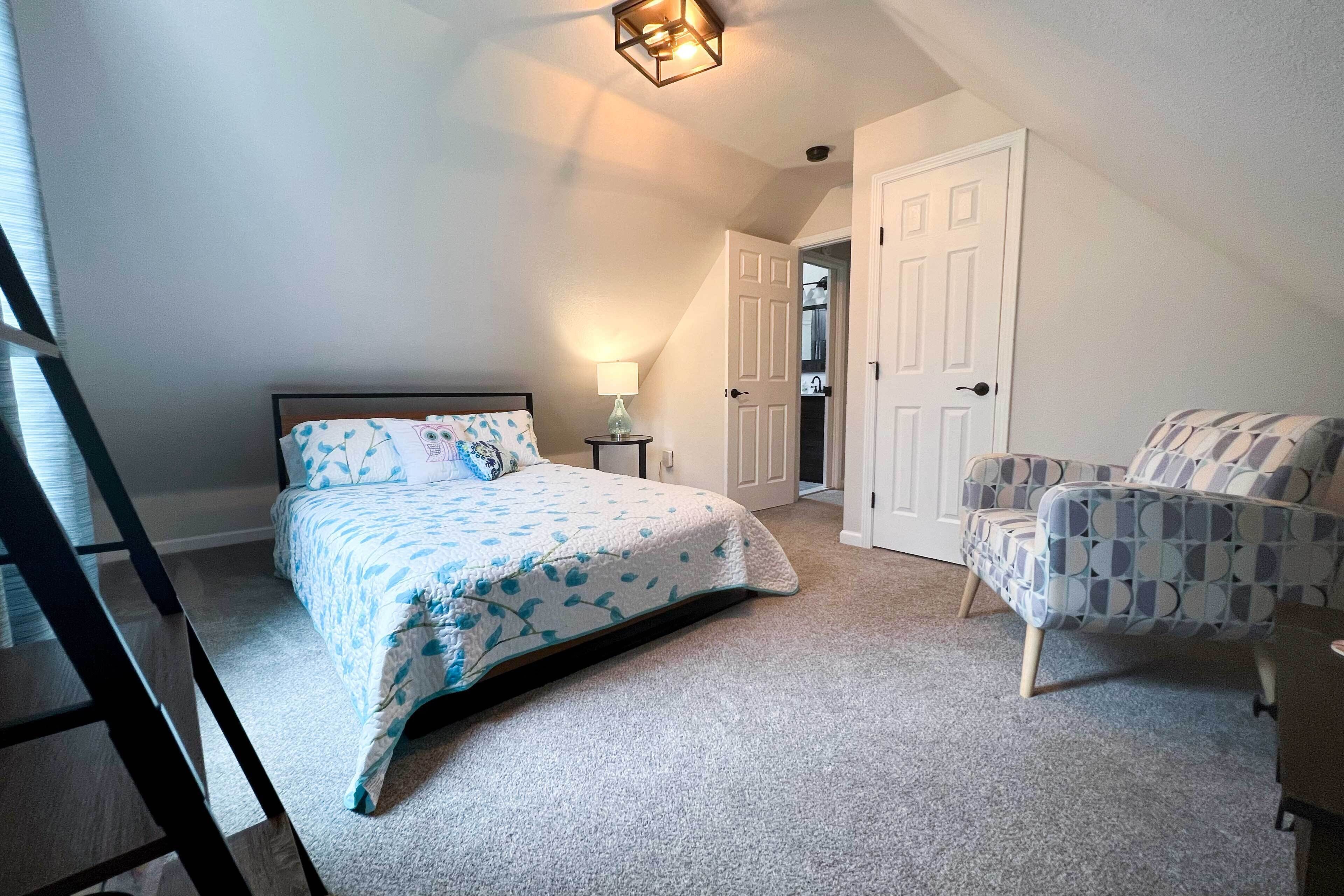 A bedroom with a bed, a chair, a nightstand, and a door leading to a bathroom.