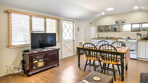 Una sala de estar con televisor, mueble de madera, mesa de comedor con sillas y una zona de cocina con electrodomésticos.