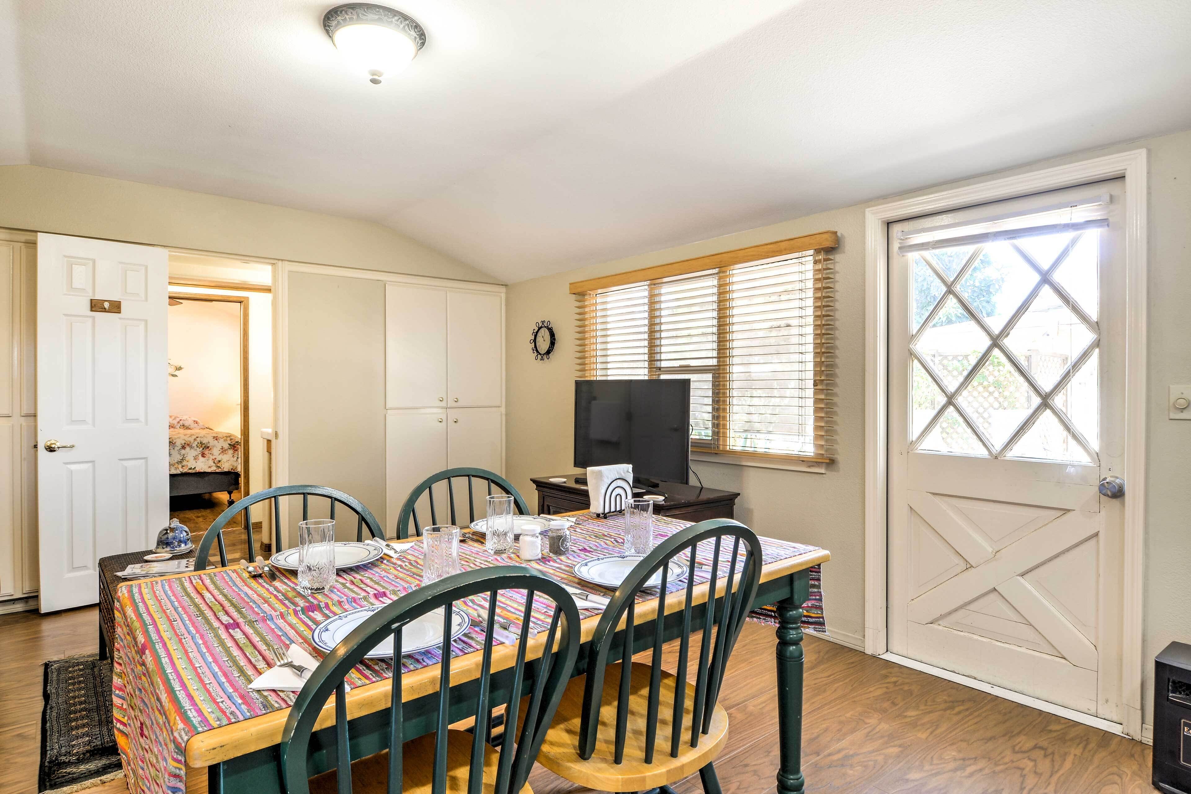 A dining area with a table set for four, a television on a stand, and a door leading to another room.