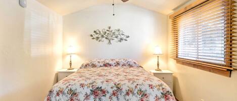 A bedroom with a ceiling fan, two bedside lamps, a floral bedspread, and a window with blinds.