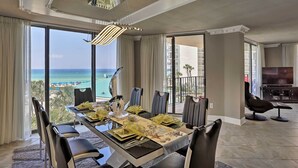 A dining area with a view of the ocean, a balcony, and a TV in the living room.