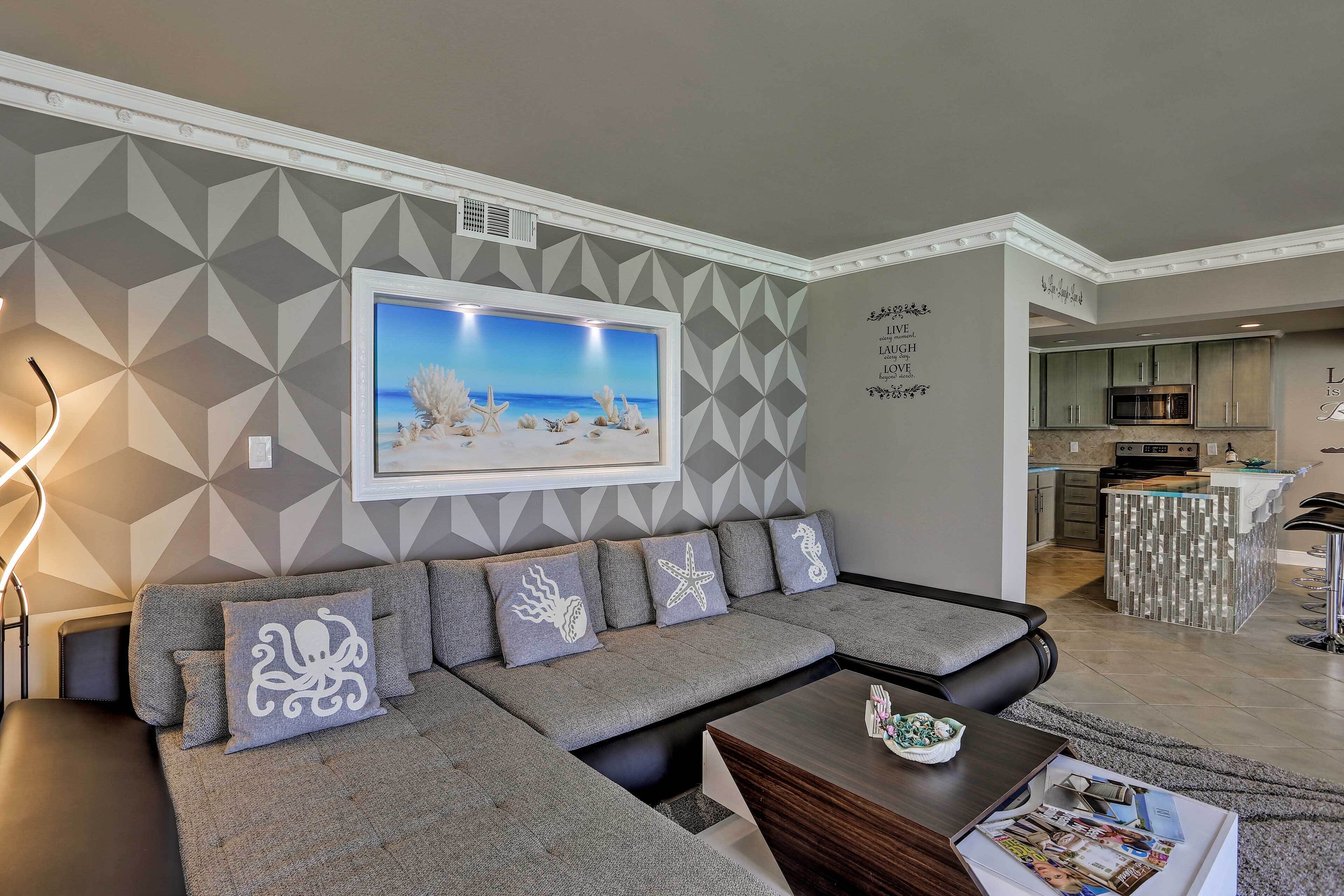 A modern living room with a grey sectional sofa, a coffee table, and a kitchen in the background.