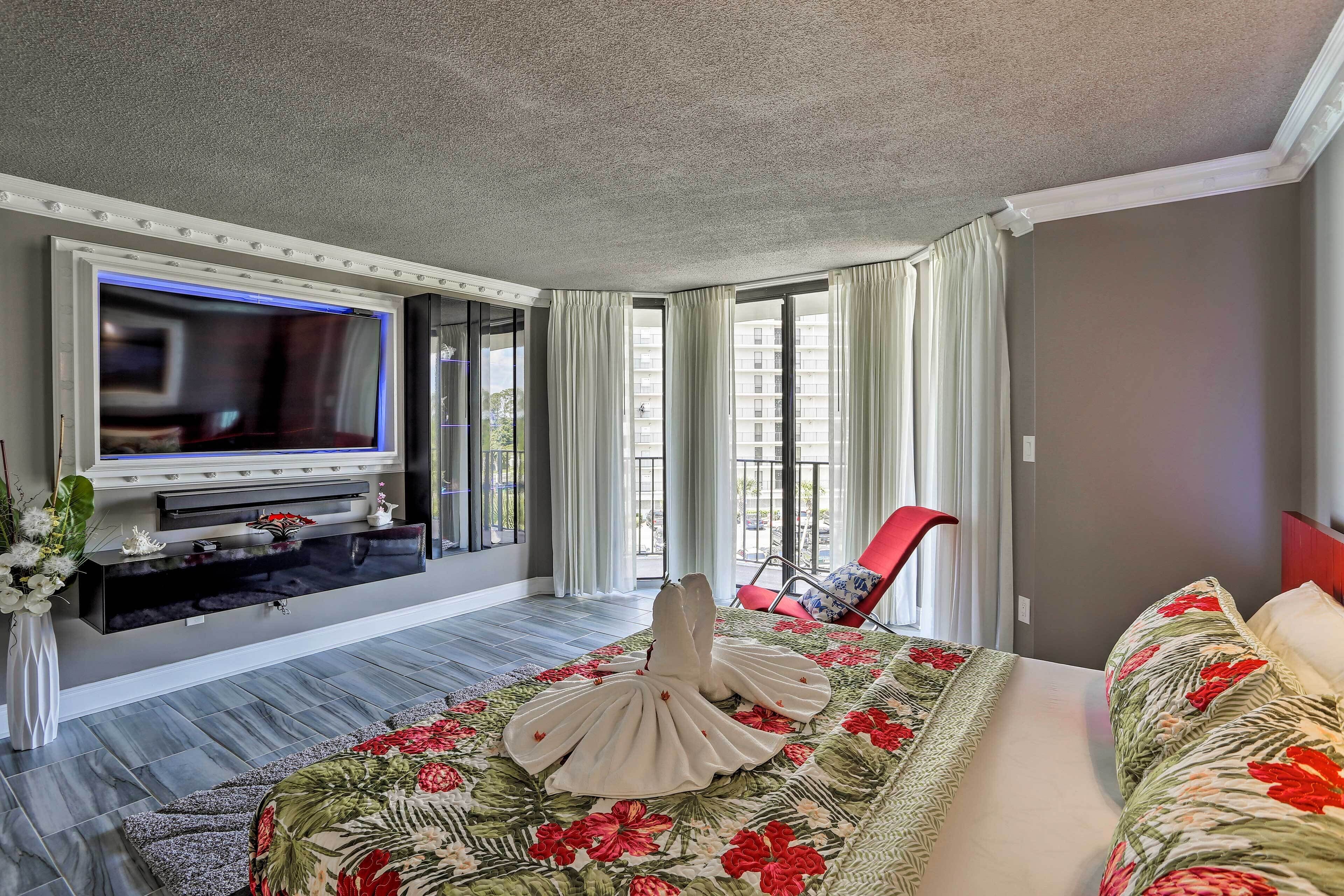 Habitación de hotel con una cama grande, un televisor de pantalla plana, una silla roja y vistas al exterior.
