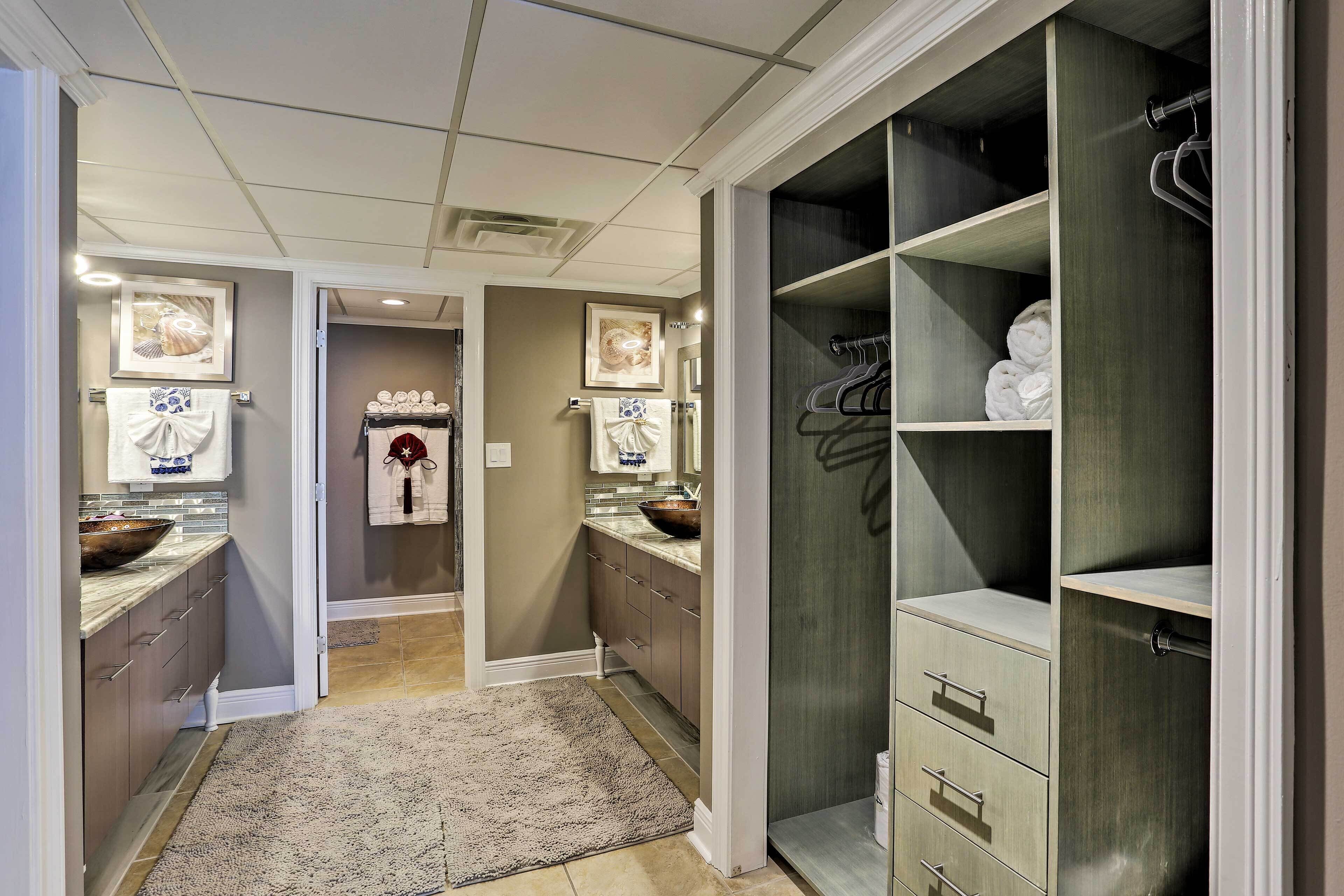 A modern bathroom with a walk-in shower, a vanity with a large mirror, and a walk-in closet with shelves and drawers.